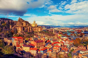 Aerial view of Tbilisi with Narikala Fortress overlooking the old city's terracotta roofs and Metekhi Church with mountains i